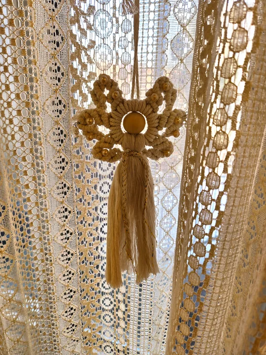 Bronze macramé angel with a ring halo, in front of a lace curtain