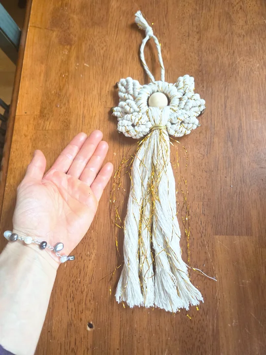 Small cream macramé angel with gold threads, beside a hand for size