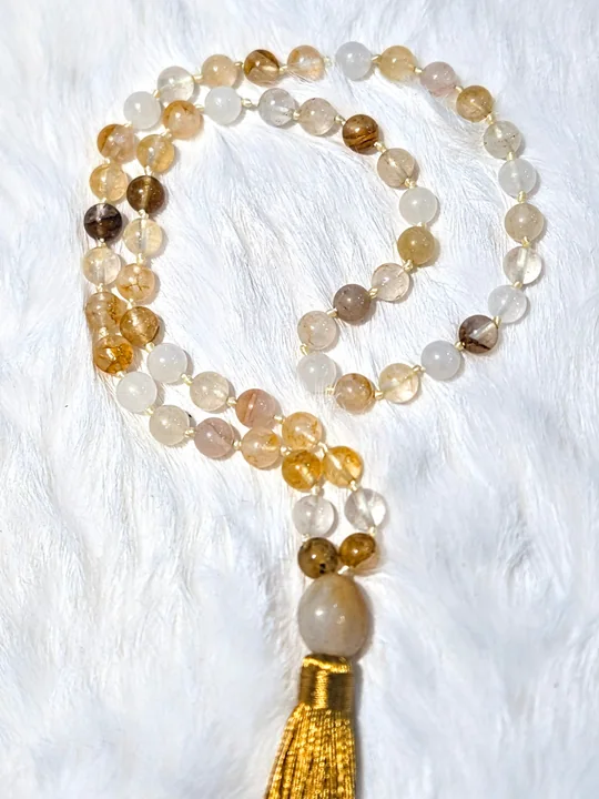 Hand-knotted mala of golden citrine and clear quartz beads with a gold silk tassel, on white fur