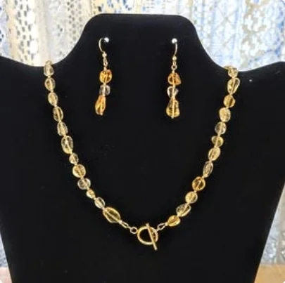 Citrine bead necklace with gold-filled beads and a gold toggle clasp, with matching citrine earrings, on a black display