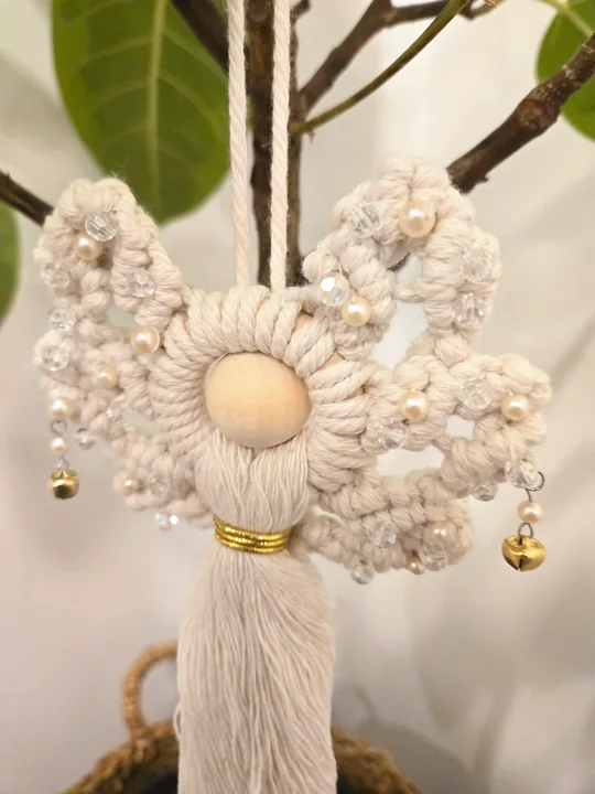 Cream macramé angel with pearls and gold bells, hanging in a ficus tree