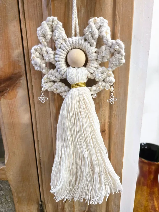 Cream macramé angel with silver flower charms, against a wooden door