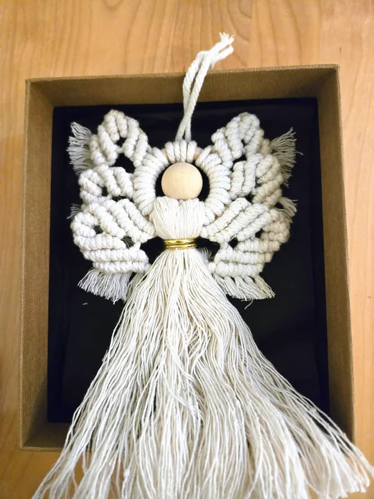 Cream macramé angel with curled wings in a black shadow box frame