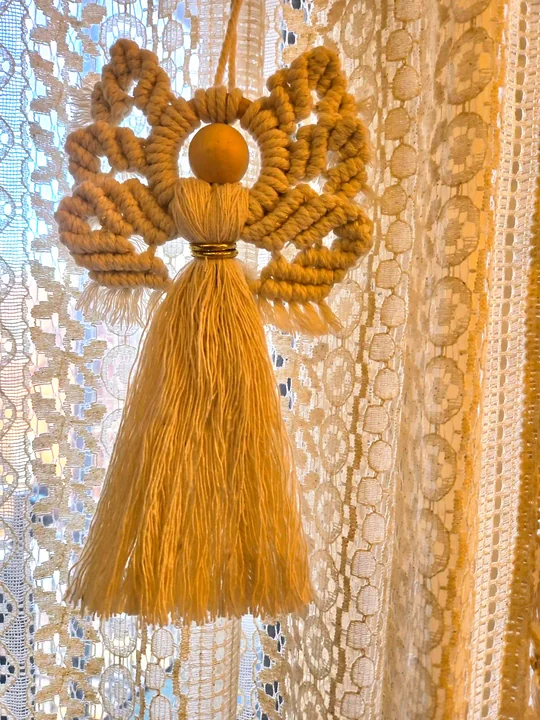 Golden mustard macramé angel in front of a lace curtain