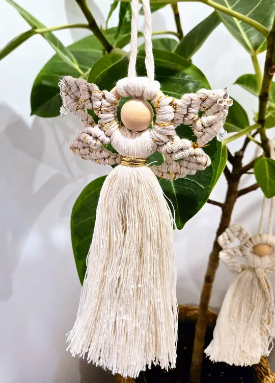 Bright white macramé angel with pearls and bells, held in front of a ficus
