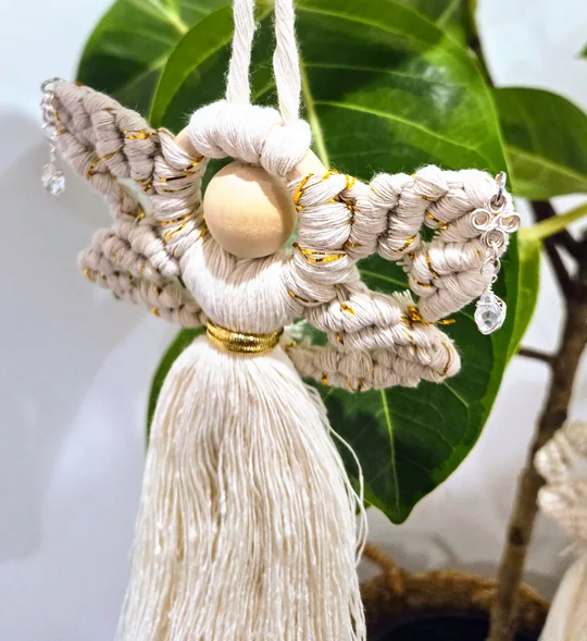 Cream macramé angel with curled wings, in front of a ficus