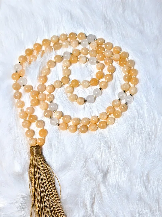 Hand-knotted mala of warm golden honey jade beads with a gold silk tassel, on white fur