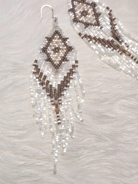 Wearing a beaded earring with a cocoa and blush diamond pattern on white and a long white fringe